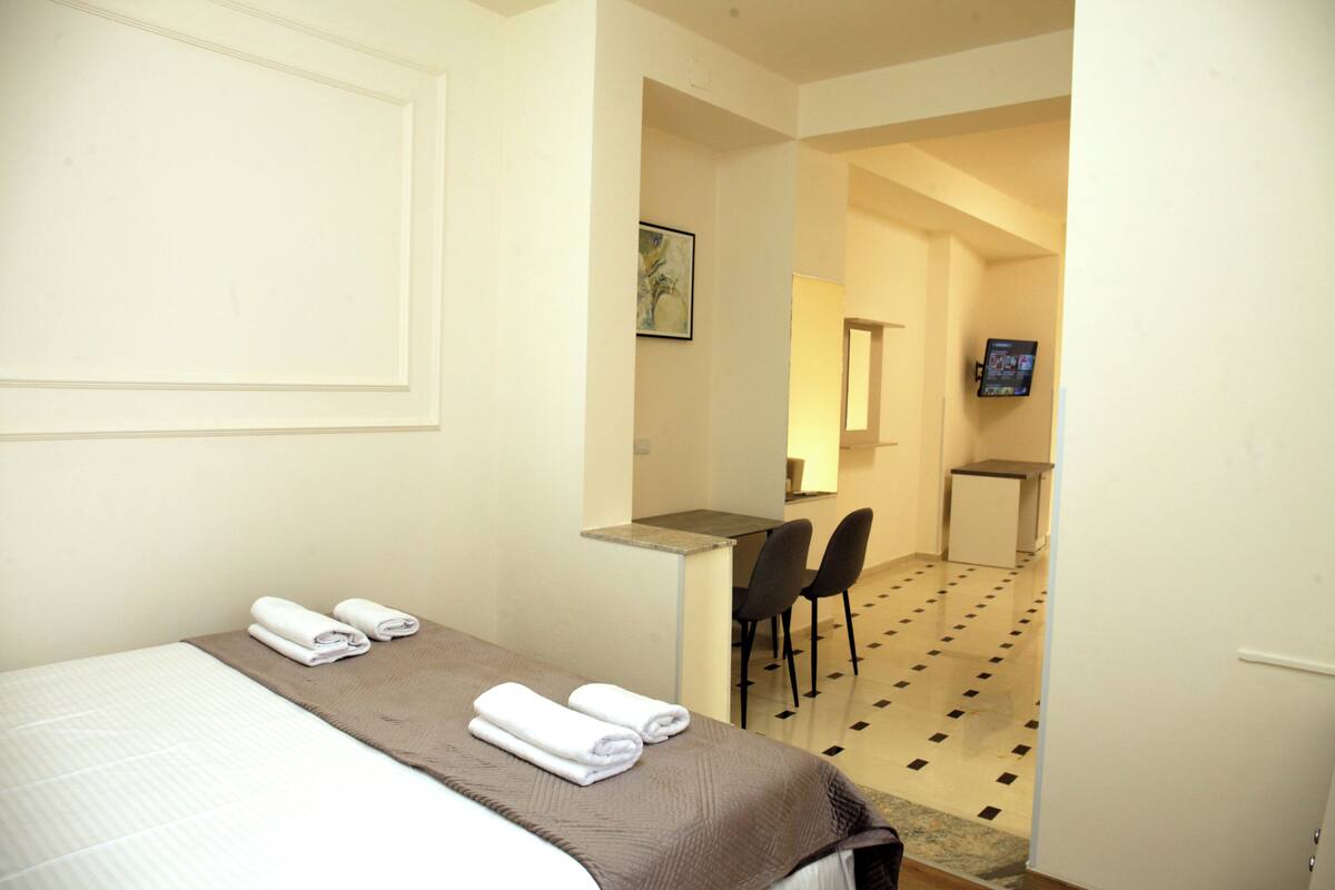 A hotel room with a bed, two chairs, a desk, and a television.