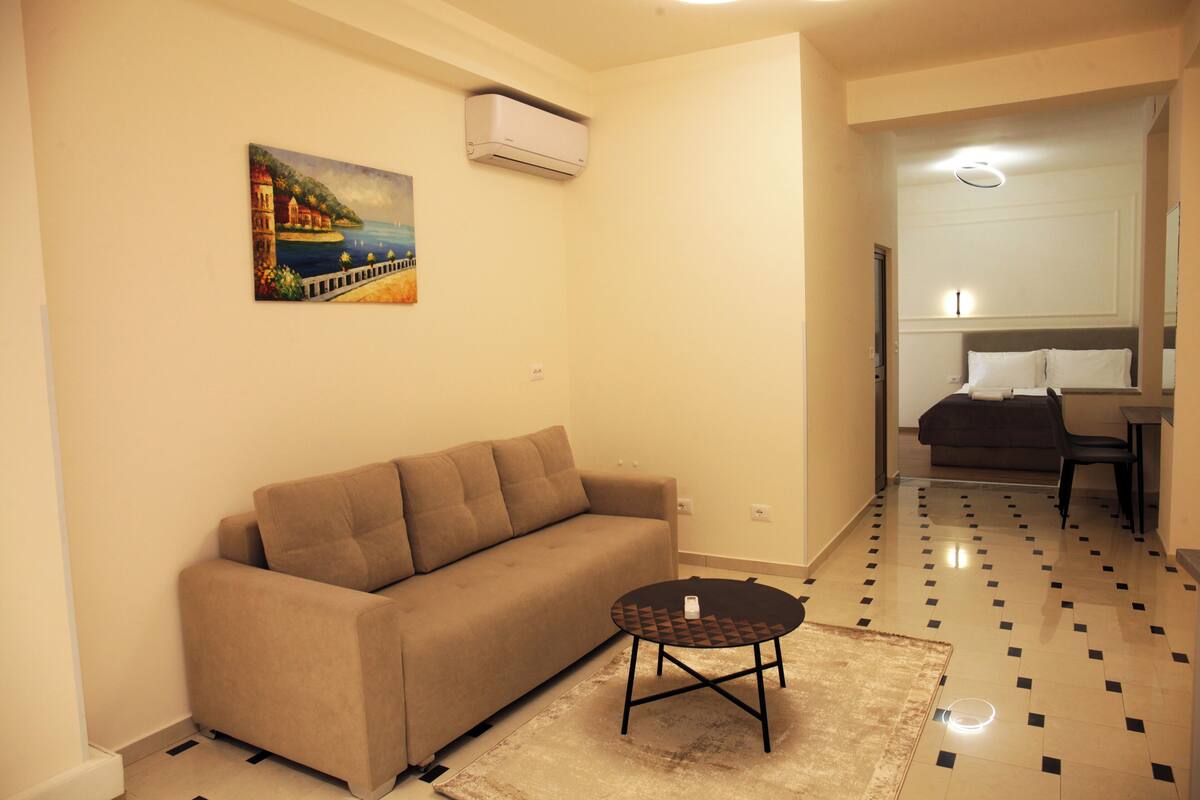 A living room with a beige sofa, a small round table, and a painting on the wall.