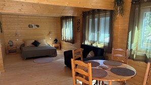 A wooden cabin interior with a bed, sofa, dining table, and chairs. - Gîte Chêne-Pin - Nature & Serenity Chalet at the Oasis des Corbières (Boutenac)