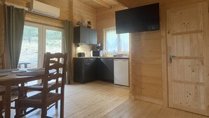 A wooden cabin interior with a dining table, chairs, a kitchen area with appliances, and a large door. - Gîte Chêne-Pin - Nature & Serenity Chalet at the Oasis des Corbières (Boutenac)