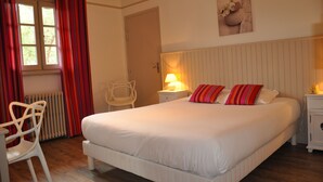 Een slaapkamer met een groot bed, een stoel, een nachtkastje en een raam met gordijnen.