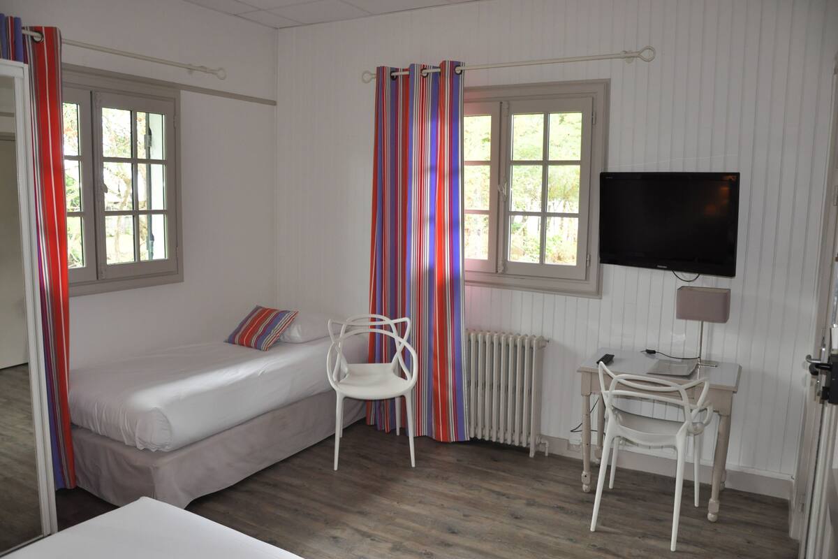 Een kamer met een bed, een bureau met stoel, een televisie en een raam met gordijnen.
