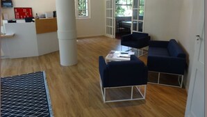 Een moderne kantoorruimte met een receptiebalie, twee blauwe stoelen, een kleine tafel en een grote zuil.