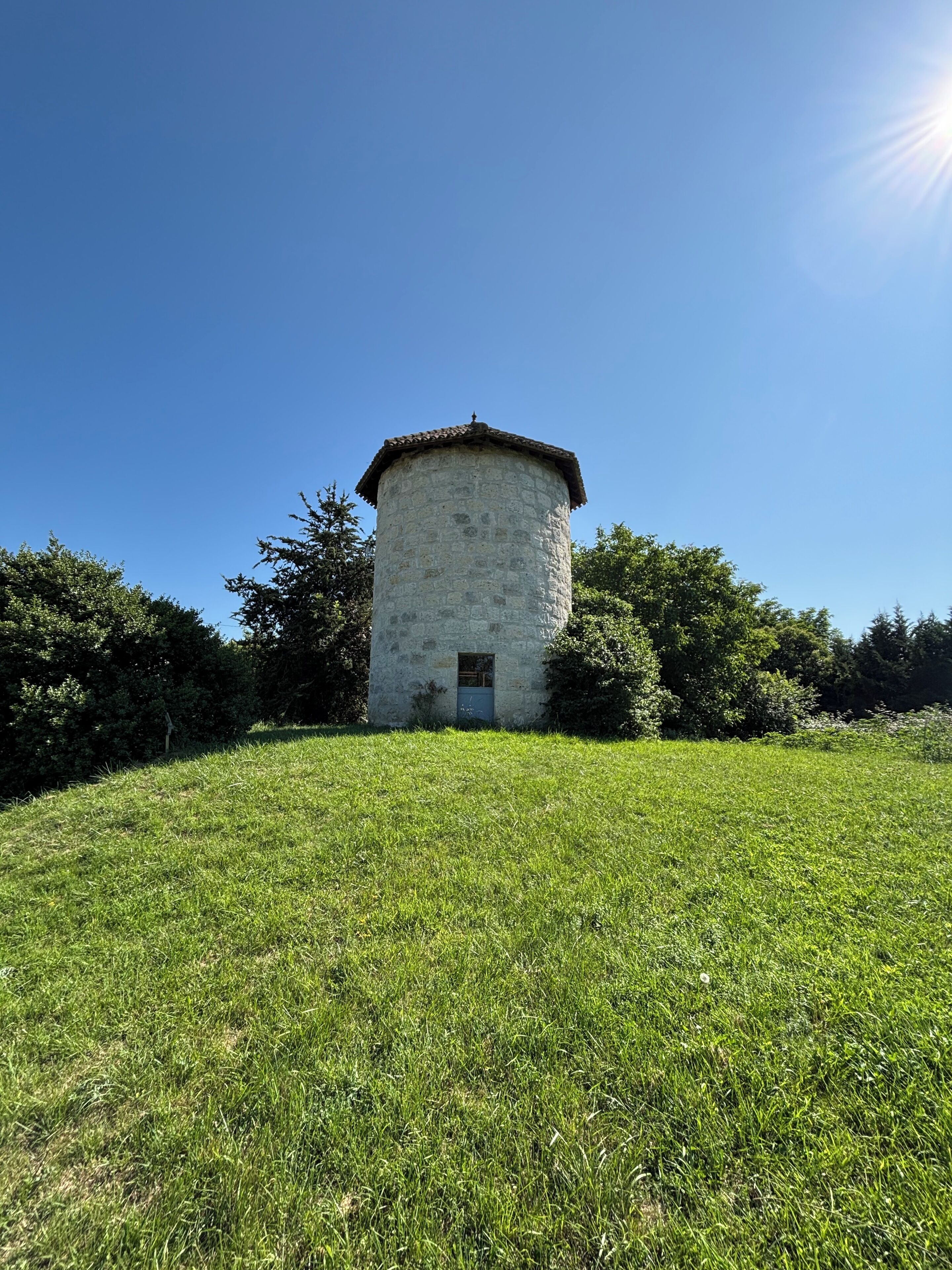 A stone tower with a small door, surrounded by a grassy field and trees.
