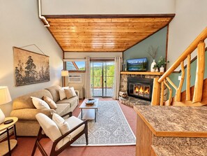 A cozy living room with a fireplace, a sofa, a coffee table, and a view of the outdoors. - Mountainside Ski-In/Ski-Out | Pool & Hot Tub (Lutsen)
