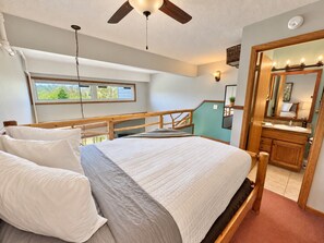 A bedroom with a bed, a ceiling fan, a window, and a bathroom with a mirror and sink. - Mountainside Ski-In/Ski-Out | Pool & Hot Tub (Lutsen)