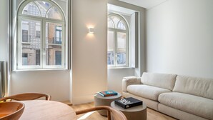 Un salon moderne avec un canapé beige, une table basse ronde et deux fenêtres surmontées d’arcs.