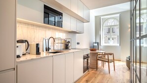 Une cuisine moderne avec des meubles blancs, une machine à café Bosch, un four à micro-ondes et une fenêtre donnant sur des immeubles.