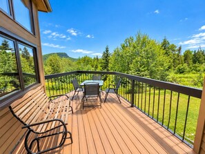 Une terrasse en bois avec une table et des chaises, offrant une vue sur un paysage verdoyant et luxuriant.