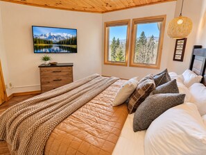 Une chambre à coucher avec un lit, une commode, un téléviseur et deux fenêtres.