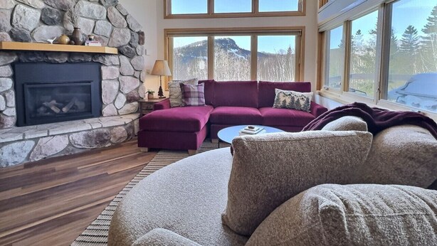 A cozy living room with a stone fireplace, large windows, and a comfortable seating area. - Family-Friendly Ski-In/Ski-Out | In-Unit Sauna (Lutsen)