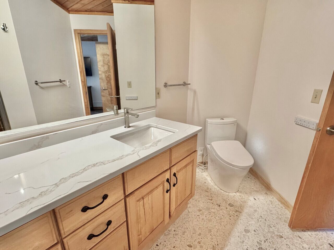 Ein Badezimmer mit Marmorwaschtisch, Holzschränken, Toilette und Spiegel.