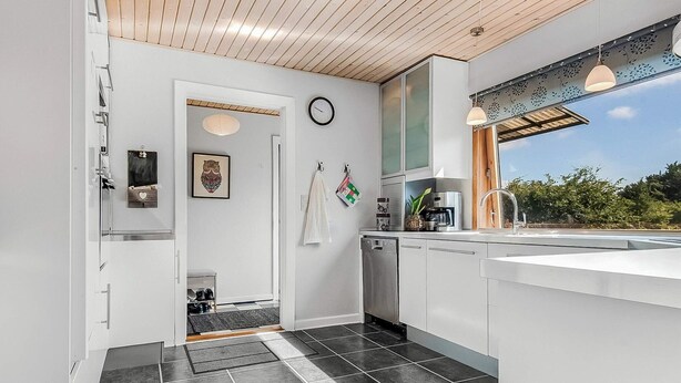 Una cocina moderna con techo de madera, lavavajillas integrado y ventana con vistas a la vegetación.