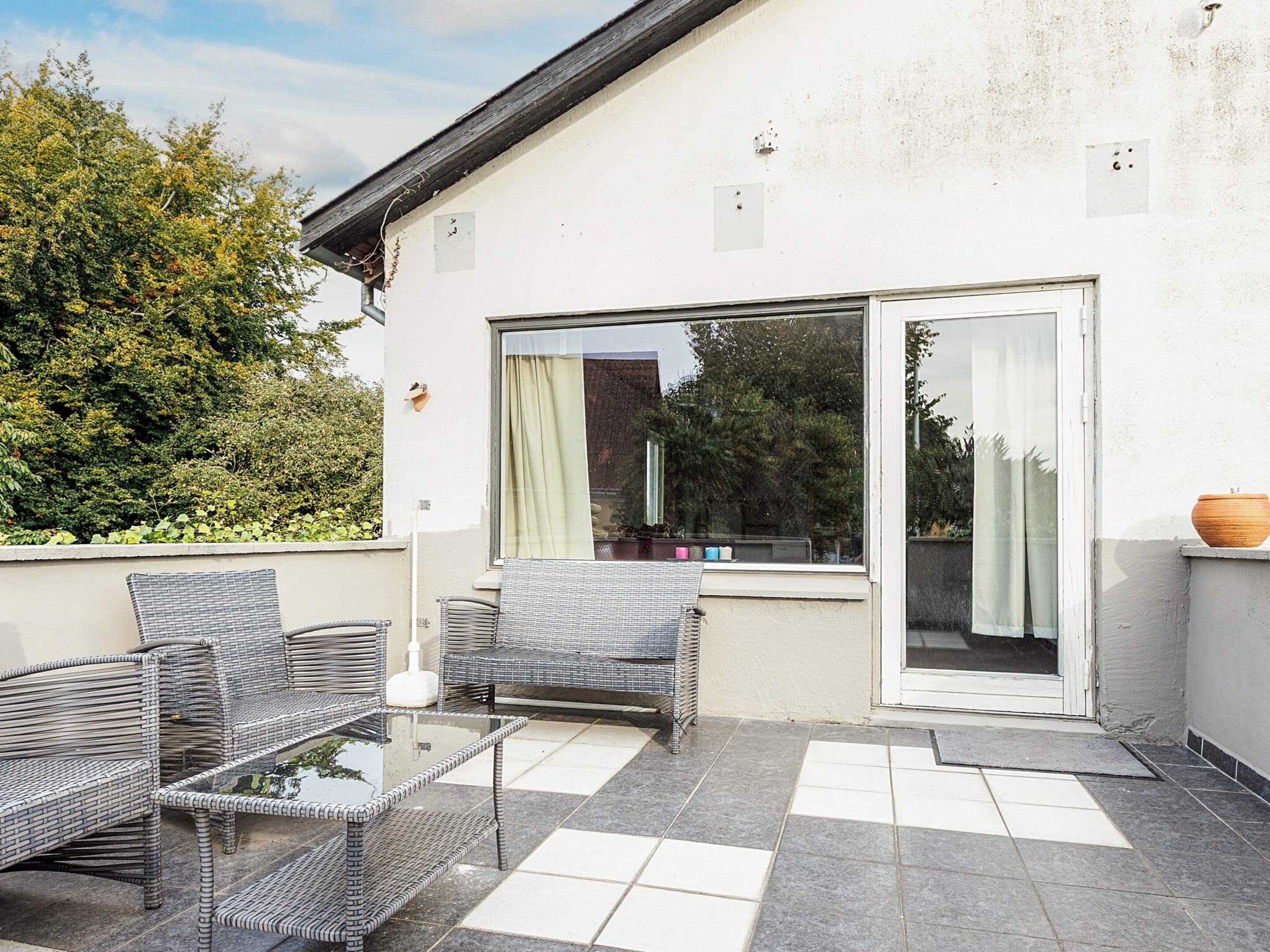 A patio area with outdoor furniture, a glass door leading to a covered space, and a view of the surrounding greenery.