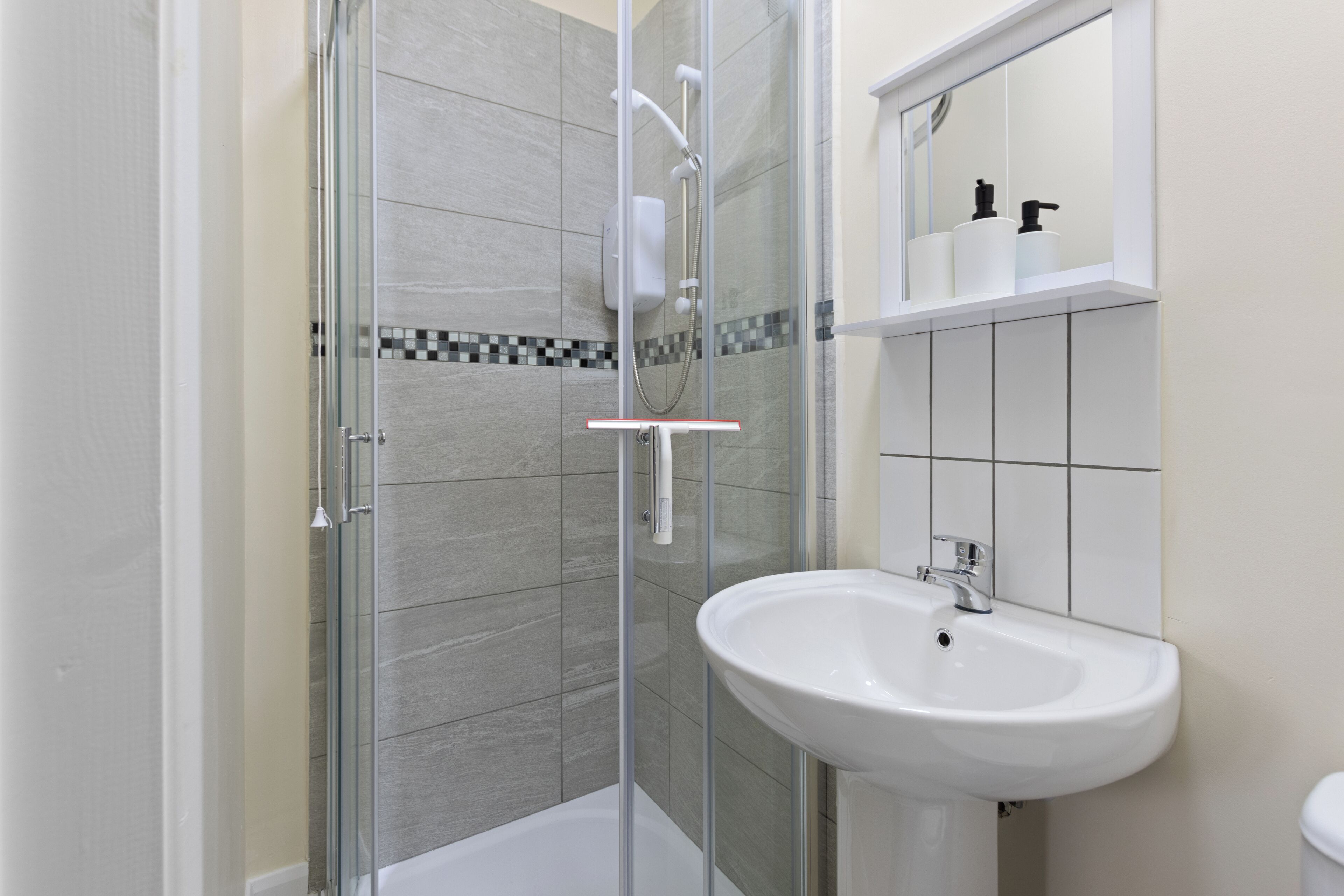 A modern bathroom with a glass-enclosed shower, a white sink, and a tiled backsplash.