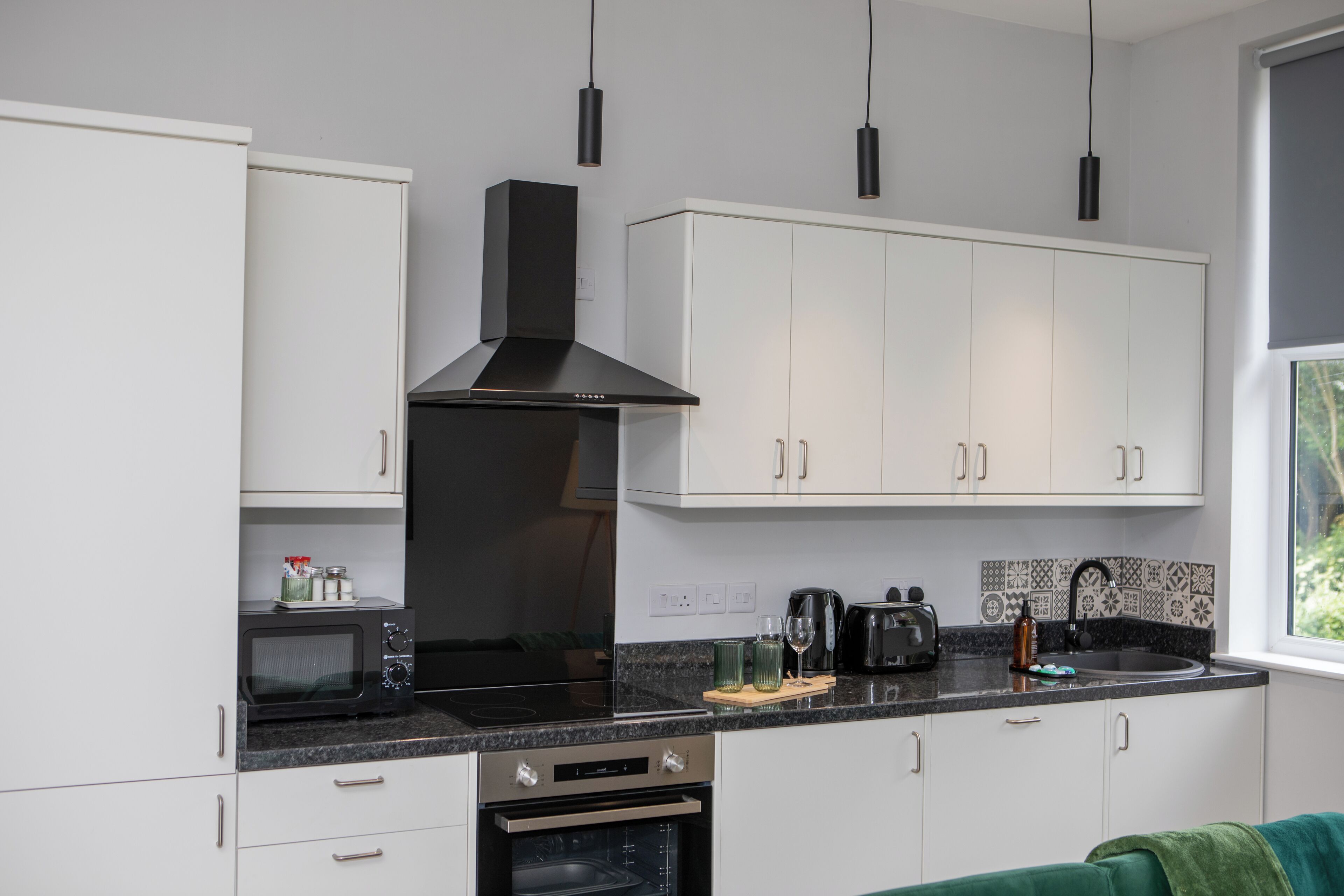 A modern kitchen with white cabinets, a black stove, and a window with a view of greenery.