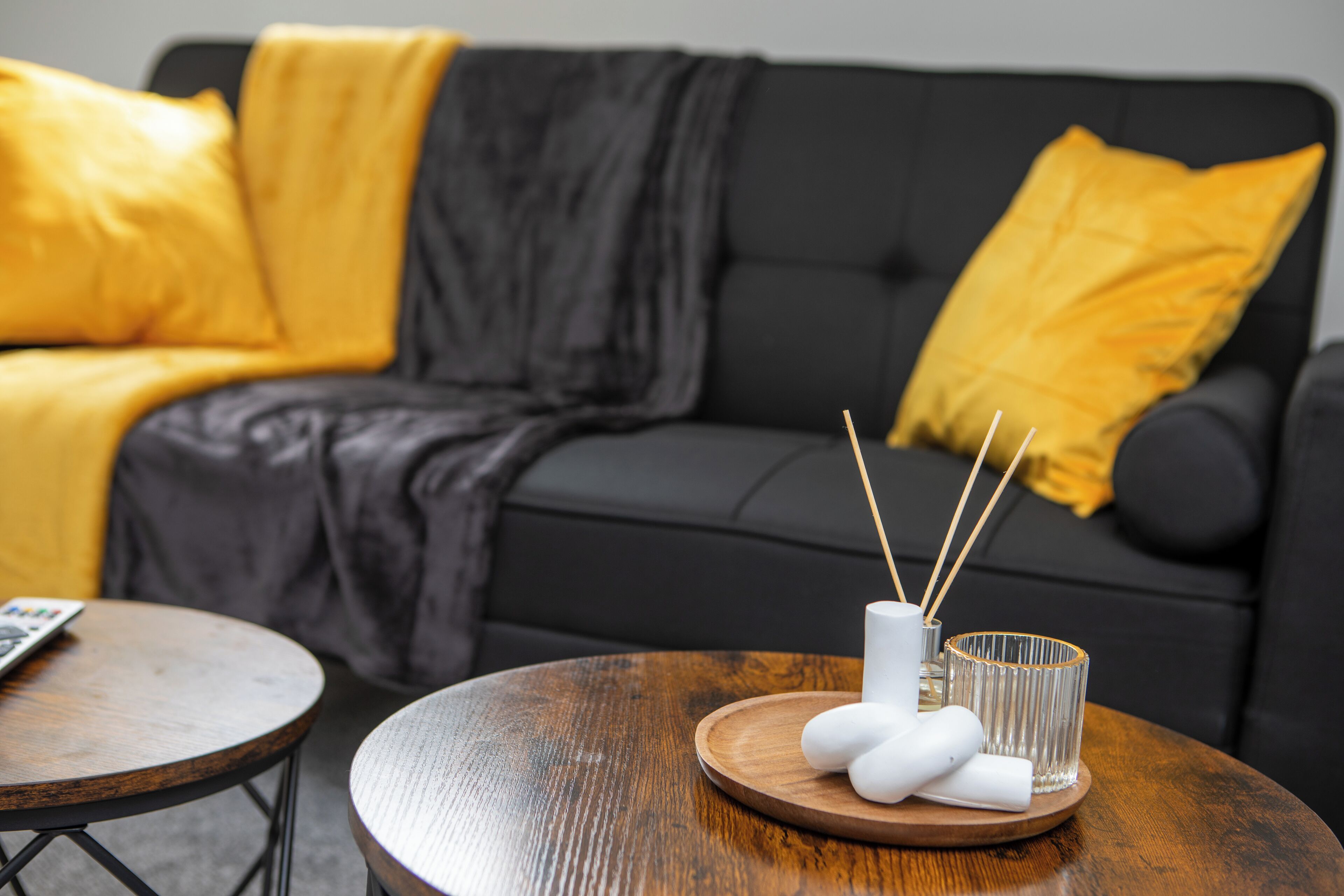 Een moderne woonkamer met een zwarte bank, gele kussens, een houten salontafel en een glazen kandelaar.
