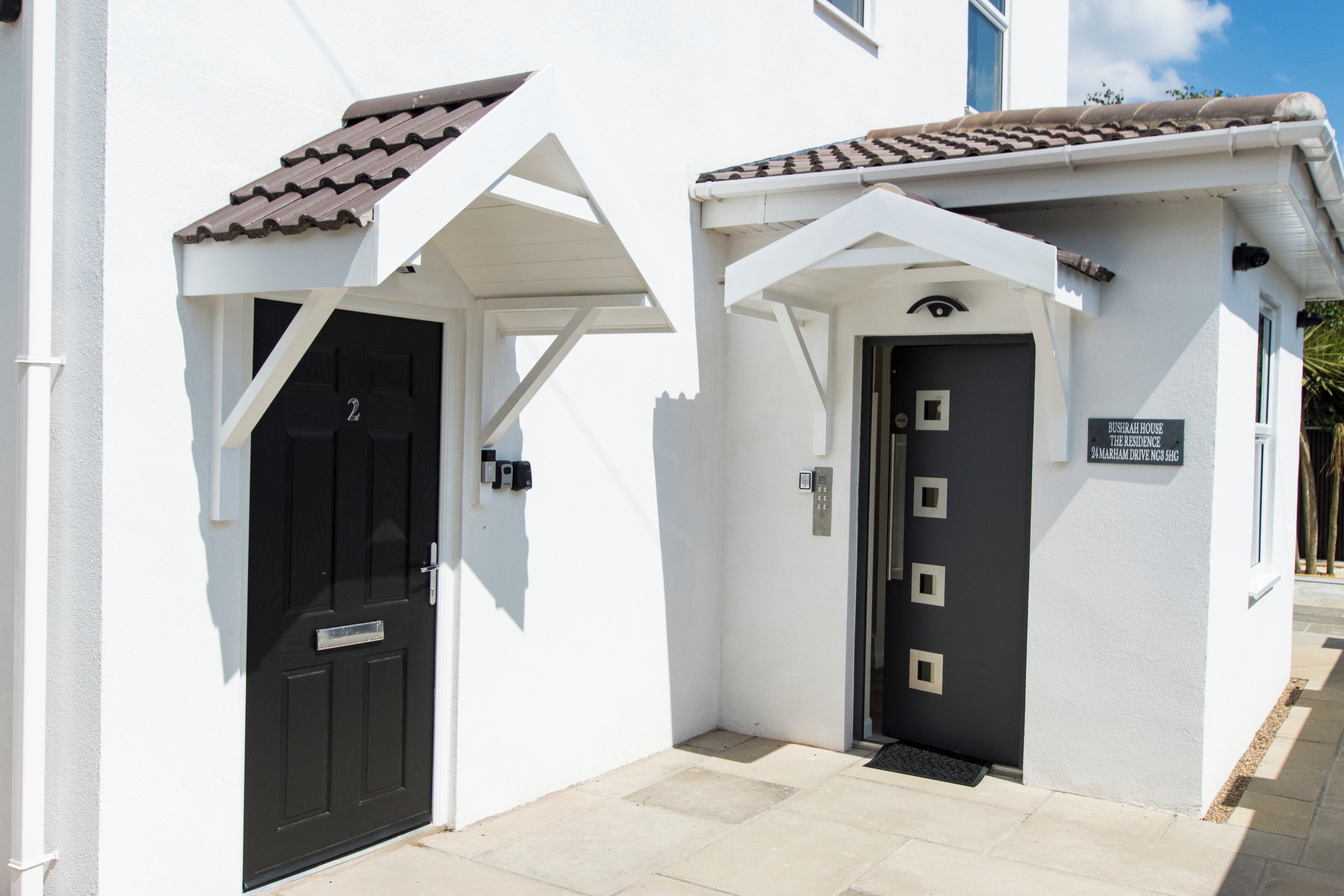 A white building with two black doors, one with a small porch and a sign above it.