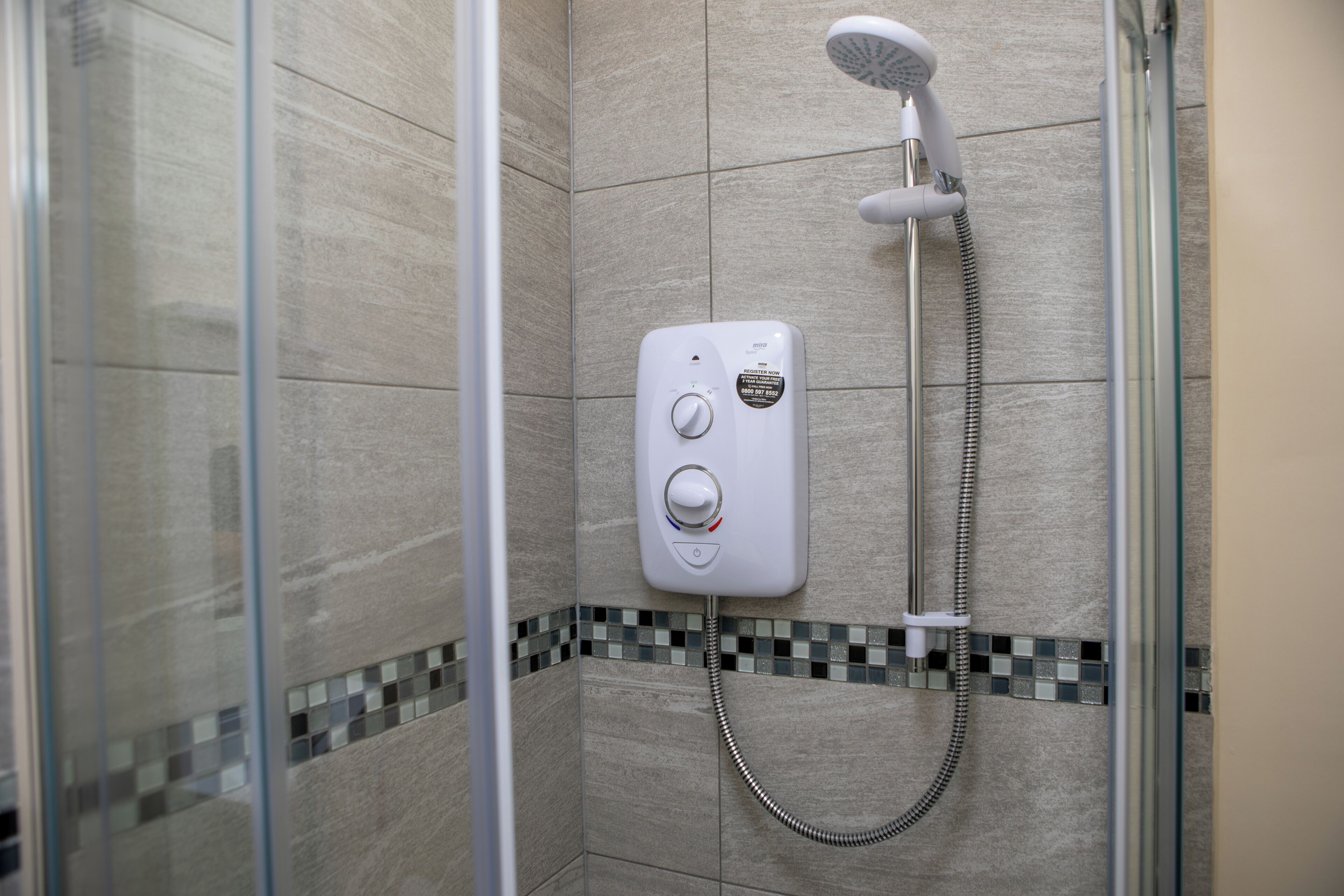 A shower with a control panel, a handheld showerhead, and a tiled wall.