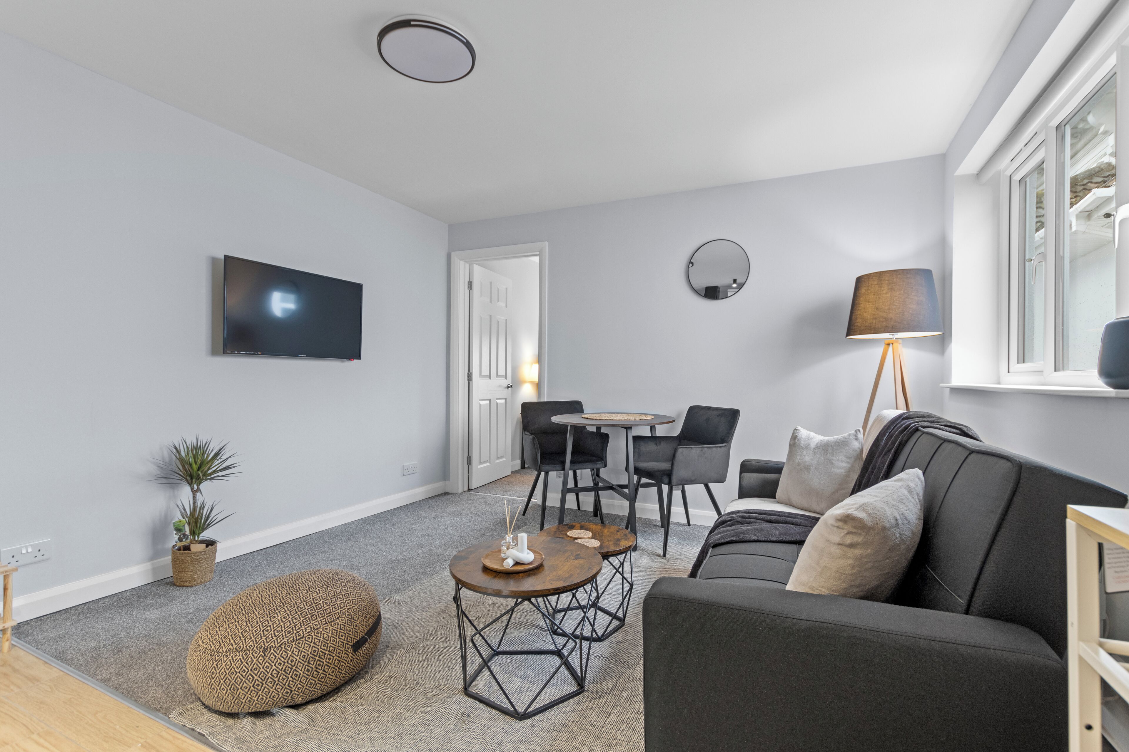 A modern living room with a grey sofa, round coffee table, and a TV mounted on the wall.