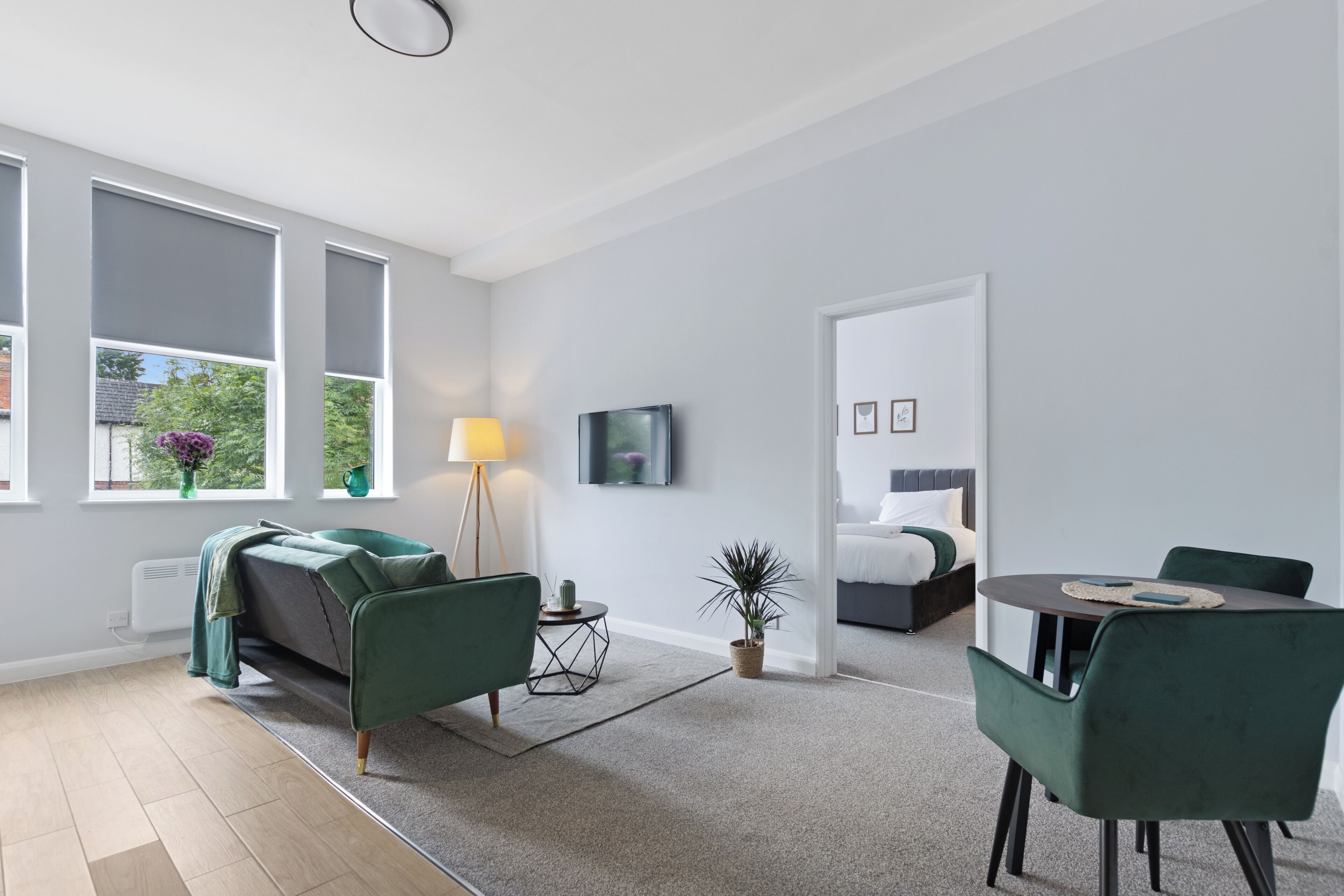 Un salon moderne avec un canapé, une table à manger et des chaises, un téléviseur fixé au mur, et un lit dans la pièce adjacente.