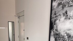 Een moderne woonkamer met een groot stadslandschap schilderij, een donkere bank met patroon kussens en een houten vloer.