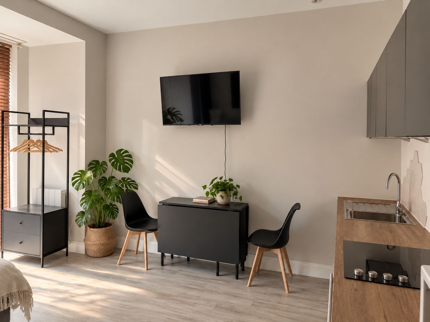 Une cuisine moderne dotée d’une cuisinière intégrée, d’un téléviseur à écran plat fixé au mur et d’un coin repas avec une table et des chaises noires.