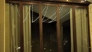 Een moderne woonkamer met een modulaire bank, een houten salontafel en grote ramen met gordijnen.
