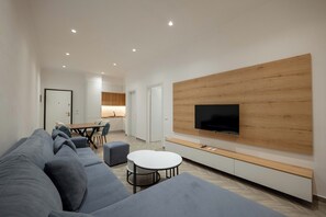 A modern living room with a large grey sofa, a white coffee table, and a flat-screen TV mounted on a wooden wall. - Regal Luxury Apartments (Sarande)
