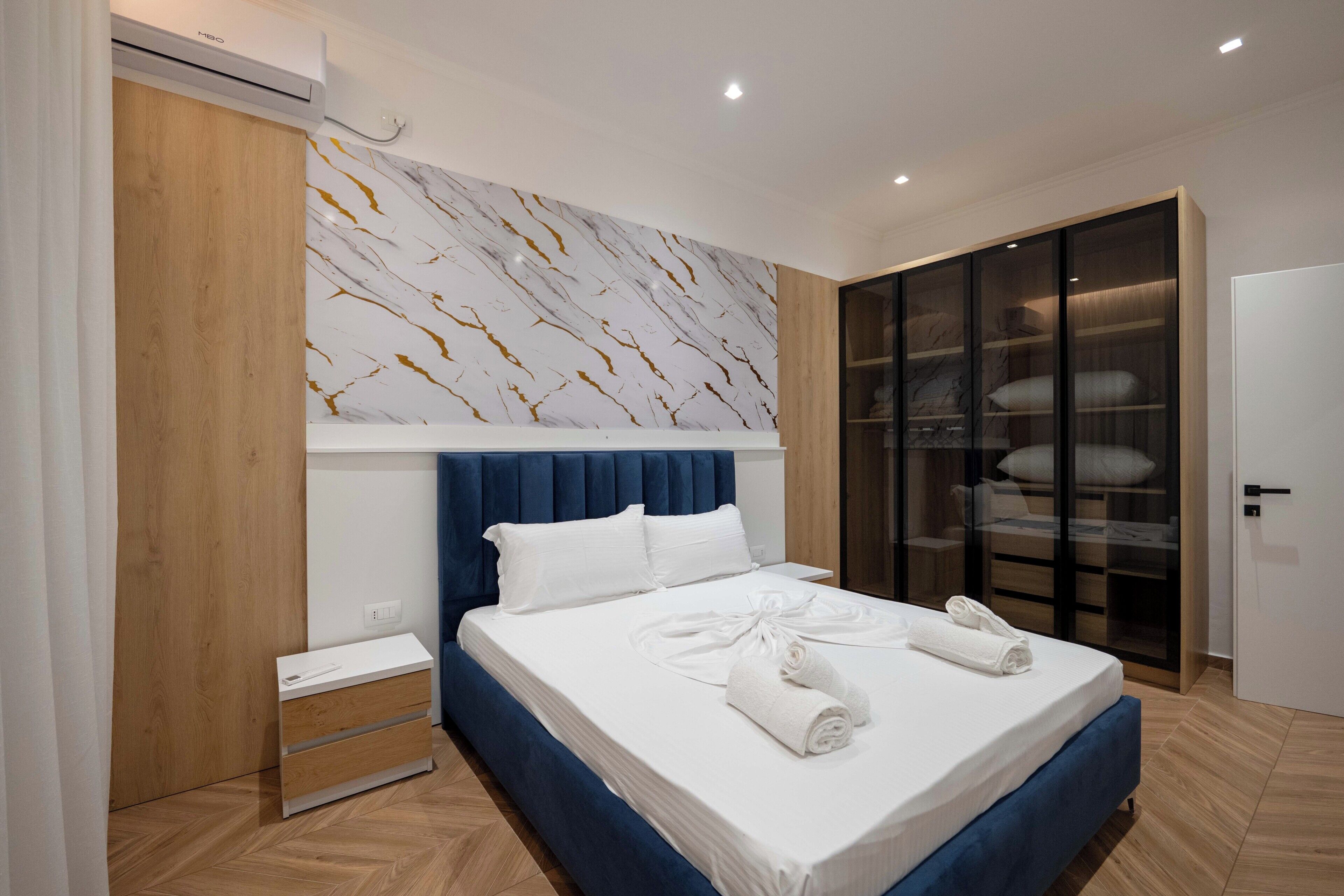 Een moderne slaapkamer met een bed, een kledingkast, een nachtkastje en een wand met een marmerlook.