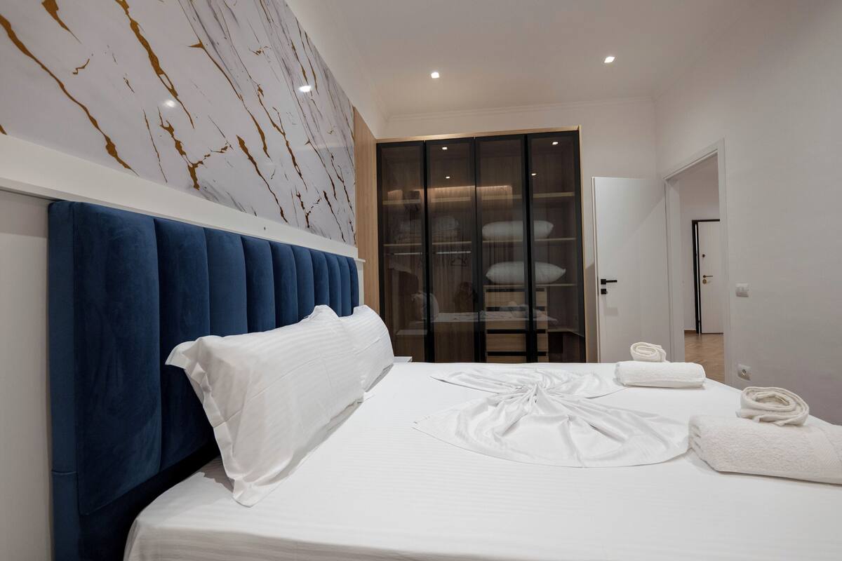 Una habitación de hotel moderna con una cama grande, un cabecero azul, un armario y una pared de mármol.