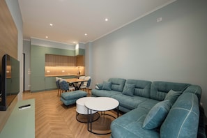 Un salon moderne avec un canapé d’angle, une table à manger avec des chaises et un téléviseur.