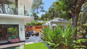 A modern house with a swimming pool, a patio with outdoor furniture, and lush greenery.