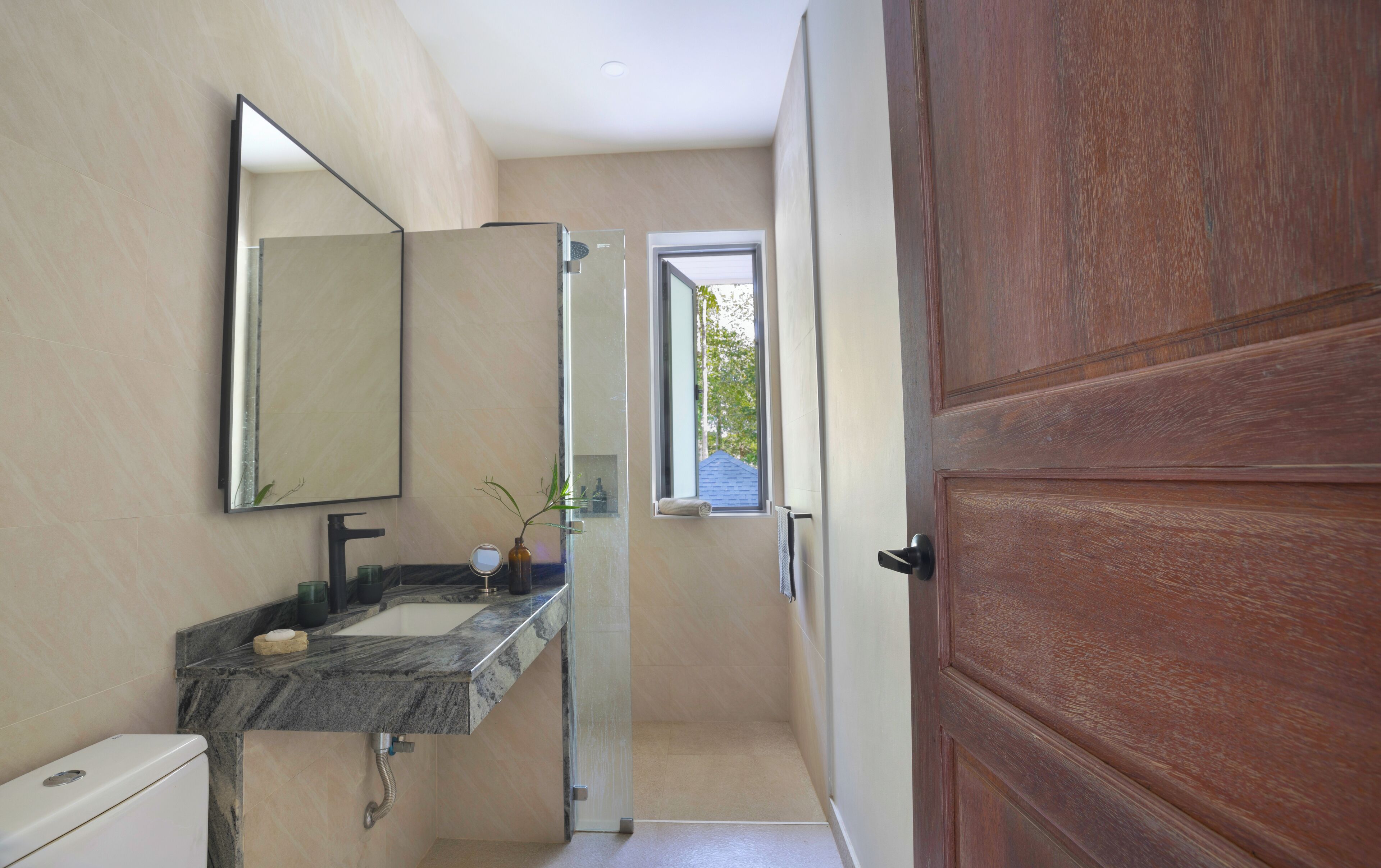 A bathroom with a marble sink, a mirror, a toilet, and a wooden door.