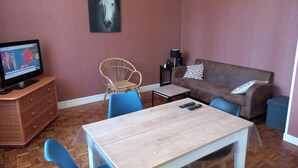 Un salon comprenant un téléviseur, un canapé, un fauteuil, une table et un tableau accroché au mur.