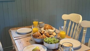 Aamiaispöydällä on croissantteja, viinirypäleitä, appelsiinimehua ja päärynä.