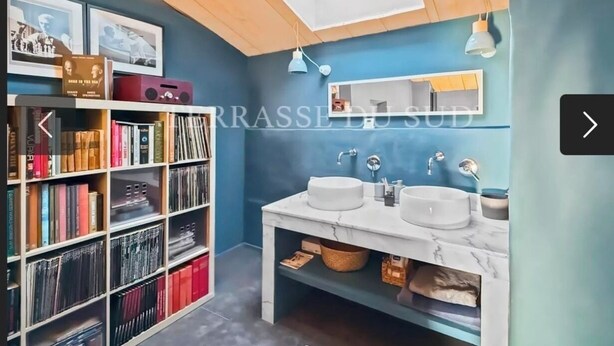 A modern bathroom with a skylight, two sinks, and a bookshelf filled with books.