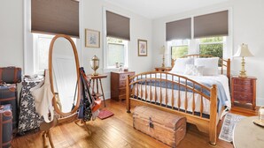 Une chambre à coucher avec un lit en bois, une commode, un miroir, une commode à tiroirs et une valise.