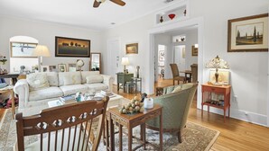 Un salon comprenant un canapé, des fauteuils, une table basse, un ventilateur de plafond et divers tableaux encadrés accrochés aux murs.