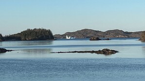 A calm body of water with a small island and a boat in the distance. - RV By The Sea. 3 Rogers Cove Rd. Cobbs Arm, NL. You, the Ocean and Mother Nature (Cobbs Arm)