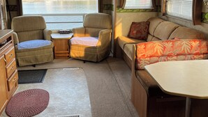 A well-lit RV interior with a seating area, a kitchenette, and a view of a lake. - RV By The Sea. 3 Rogers Cove Rd. Cobbs Arm, NL. You, the Ocean and Mother Nature (Cobbs Arm)