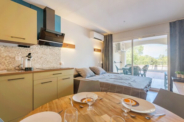A modern kitchen with a dining area, a bed, and a balcony with chairs.