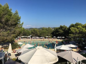 Un espace piscine agrémenté de parasols et de chaises longues, entouré d’arbres.