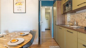 Un comedor con una mesa dispuesta para cuatro personas, una cocina equipada con microondas, y un pasillo que conduce a otra habitación.