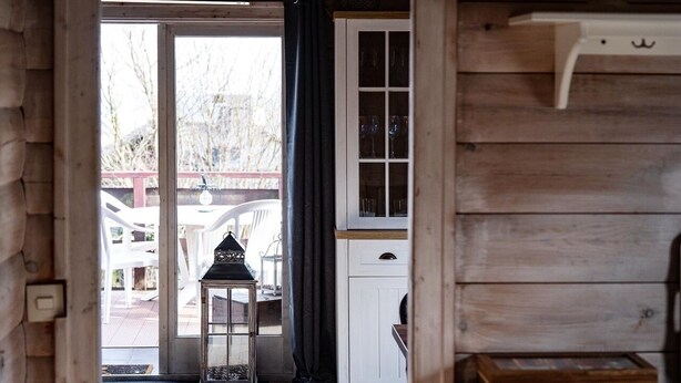 A wooden cabin interior with a glass door leading outside, a lantern, and a cabinet with glass doors.