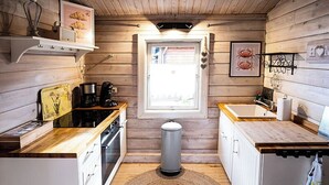 A compact kitchen with wooden walls, a central island, a window, and a trash bin.