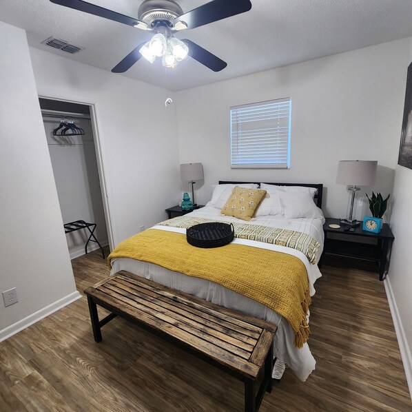 A bedroom with a bed, bedside tables, a ceiling fan, a window with blinds, a bench, and a wardrobe. - Newly renovated 2 Bed 1.5 Bath Bungalow near FAMU and FSU (Tallahassee)