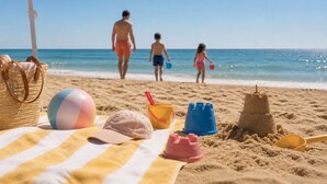 Une scène de plage avec un parasol rayé, un ballon de plage, une casquette, un château de sable et un sac de plage.