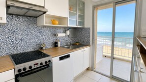 Een keuken met een fornuis, gootsteen en uitzicht op het strand door een schuifdeur.