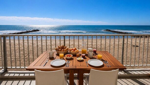 Une table en bois, dressée pour le petit-déjeuner, avec vue sur la plage et l’océan.